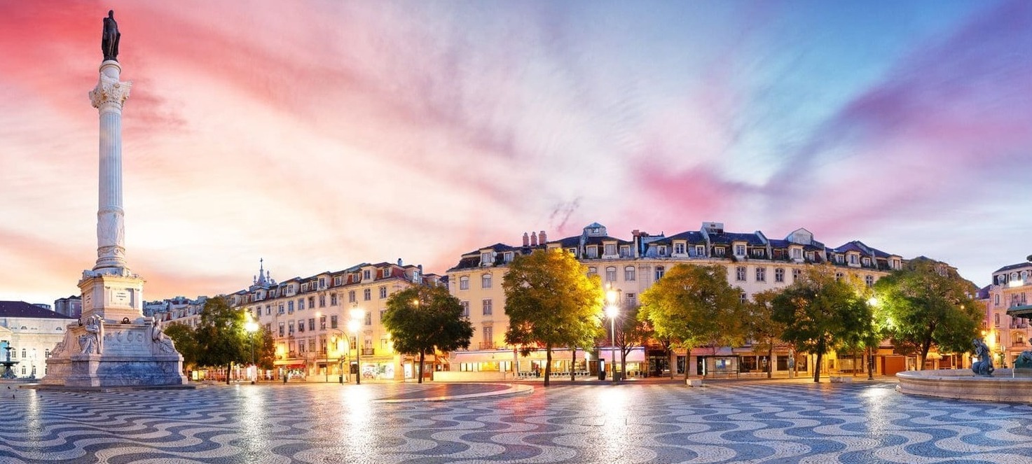 Площадь Россиу с волнообразной мозаикой на мостовой, колонной Педро IV и историческими зданиями на закате, обзорная экскурсия в Португалии.