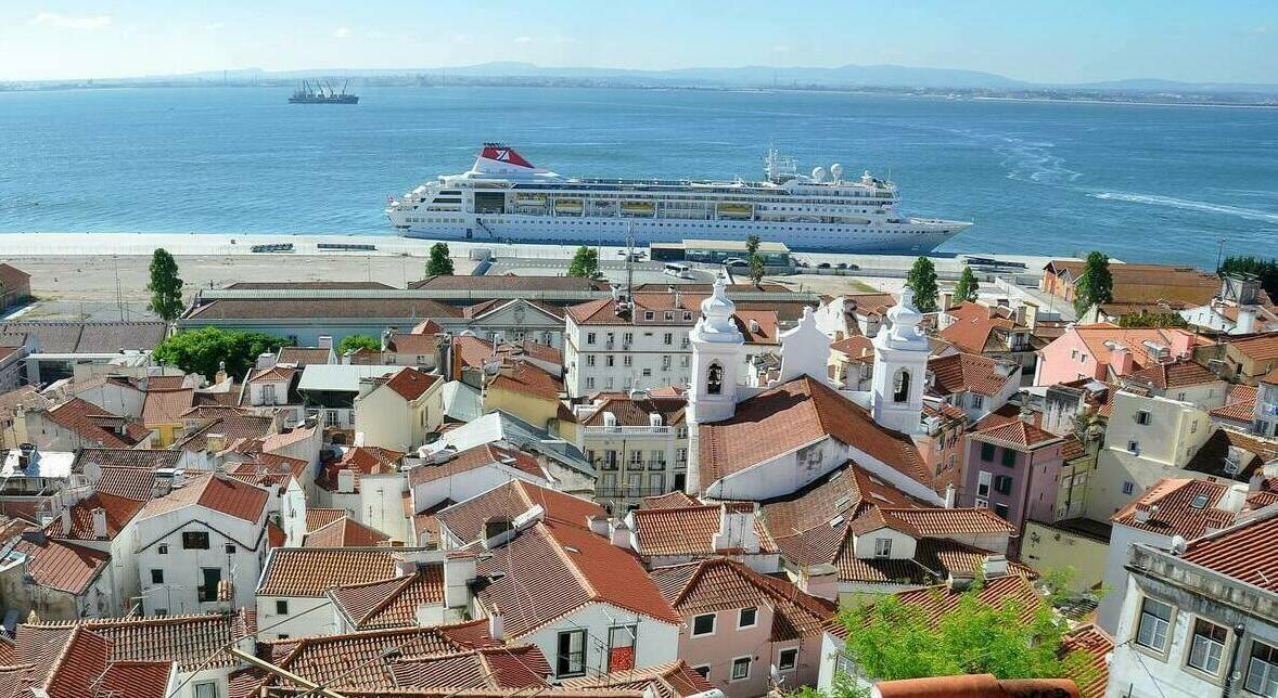Вид на красные черепичные крыши района Алфама, белые купола церквей и круизный лайнер в порту Лиссабона, экскурсии в Португалии.