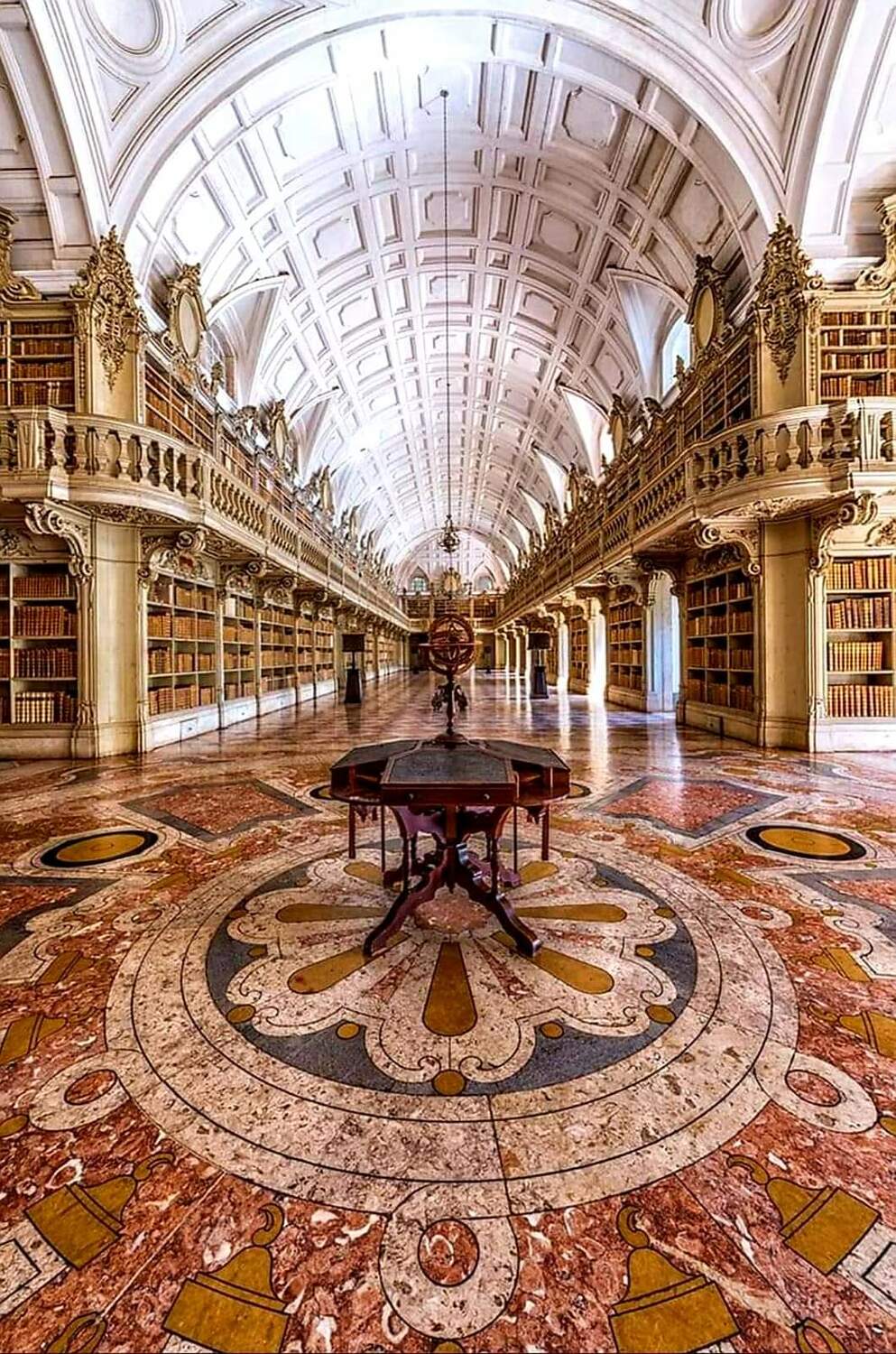 Интерьер королевской библиотеки в Мафре (Biblioteca do Palácio Nacional de Mafra), Португалия. Длинный зал в стиле рококо с белыми стеллажами и старинными глобусами.